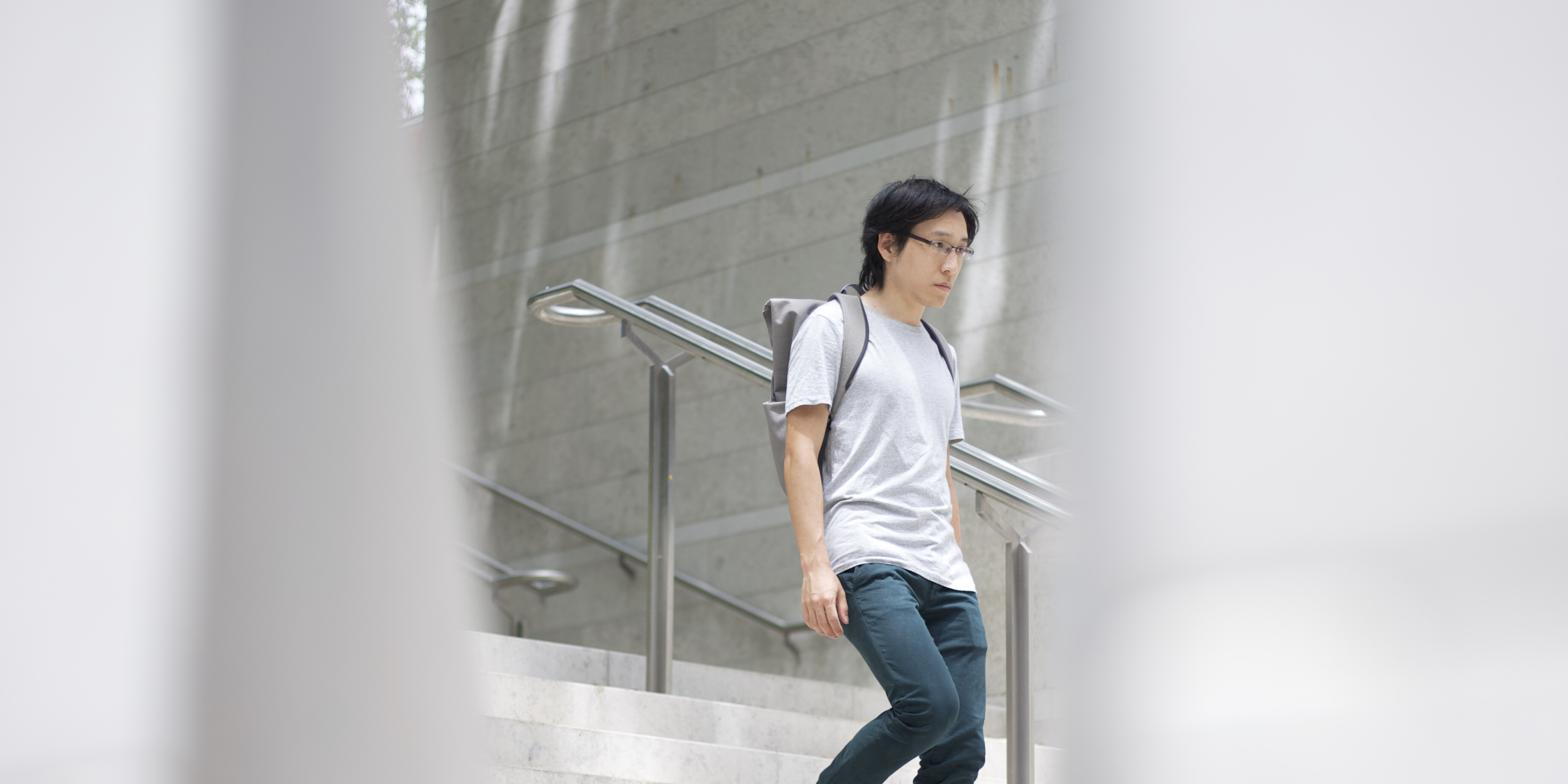 An Asian young adult walking down a marble staircase outside an art gallery.